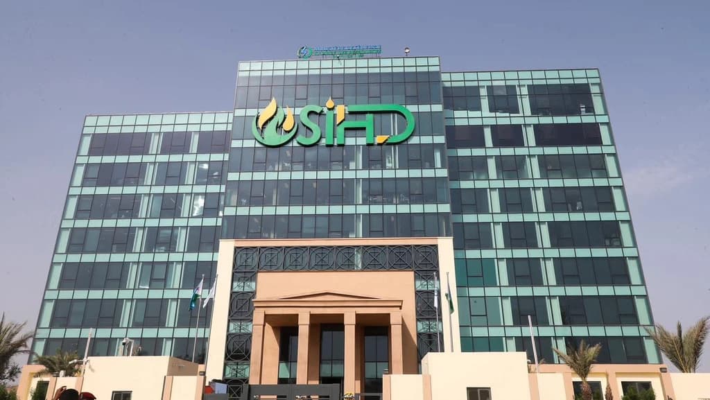 Façade vitrée vert turquoise du nouveau siège social de la SIHD, avec le logo flamme et son entrée monumentale à colonnes sous un ciel dégagé